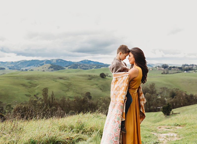 Family Photographer, Mother holds son in her arms on a grassy hillside